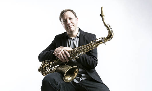 A photograph of Chris Potter holding a saxophone against a white background