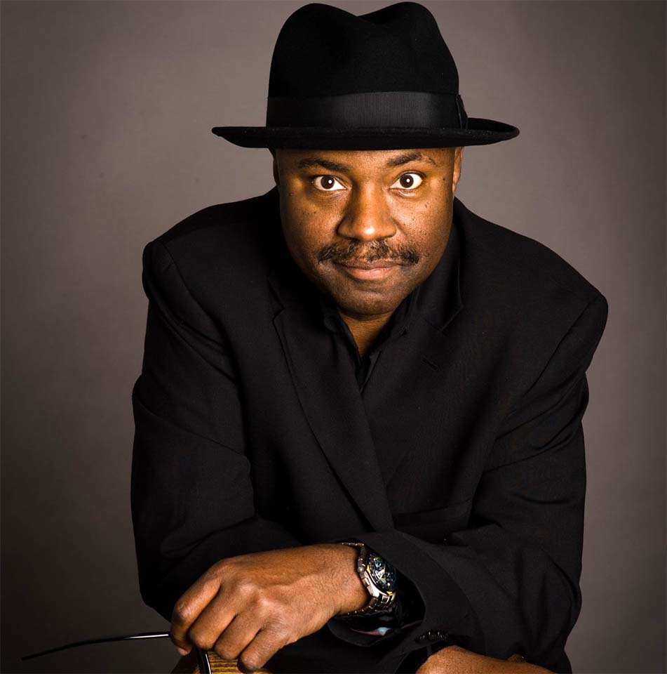 Lenny White wearing a dark suit and hat against a gray background