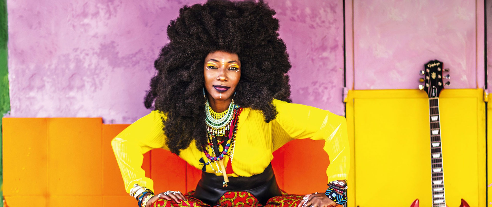 Fatoumata Diawara in vibrant dress against a pink and yellow exterior background